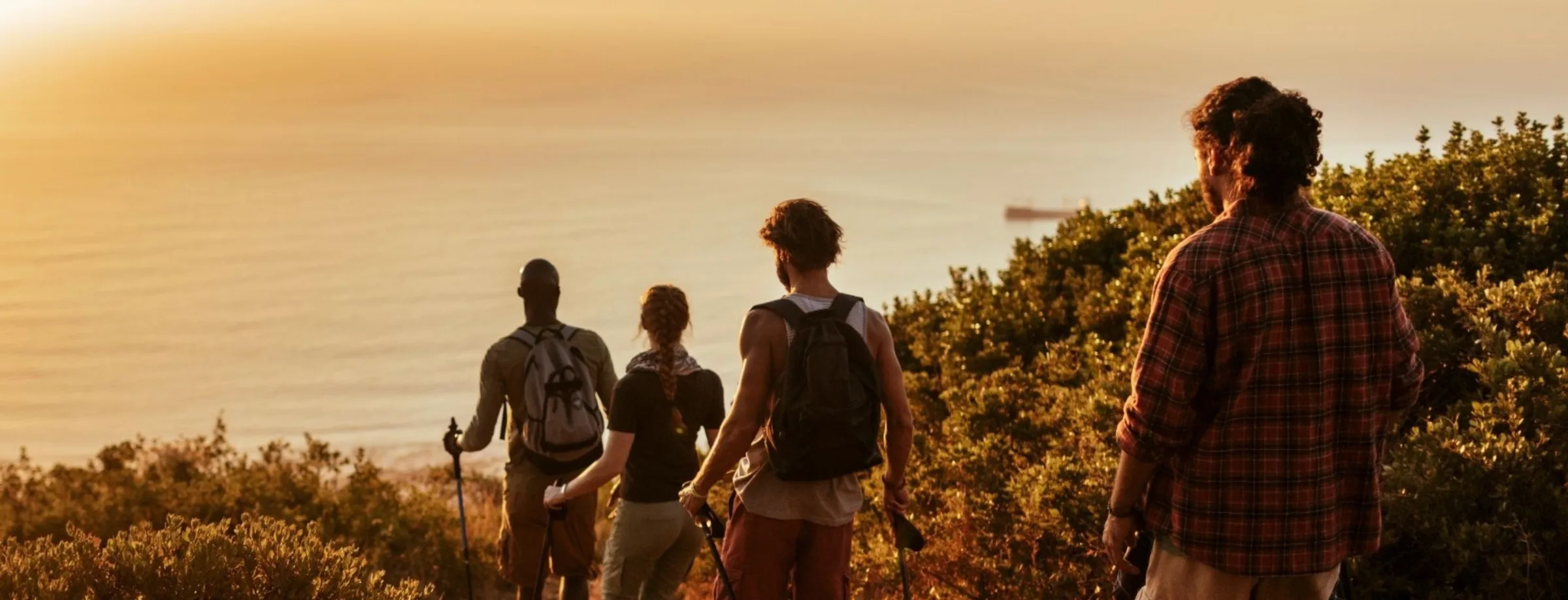 Four people walking together along a coastal trail at sunset